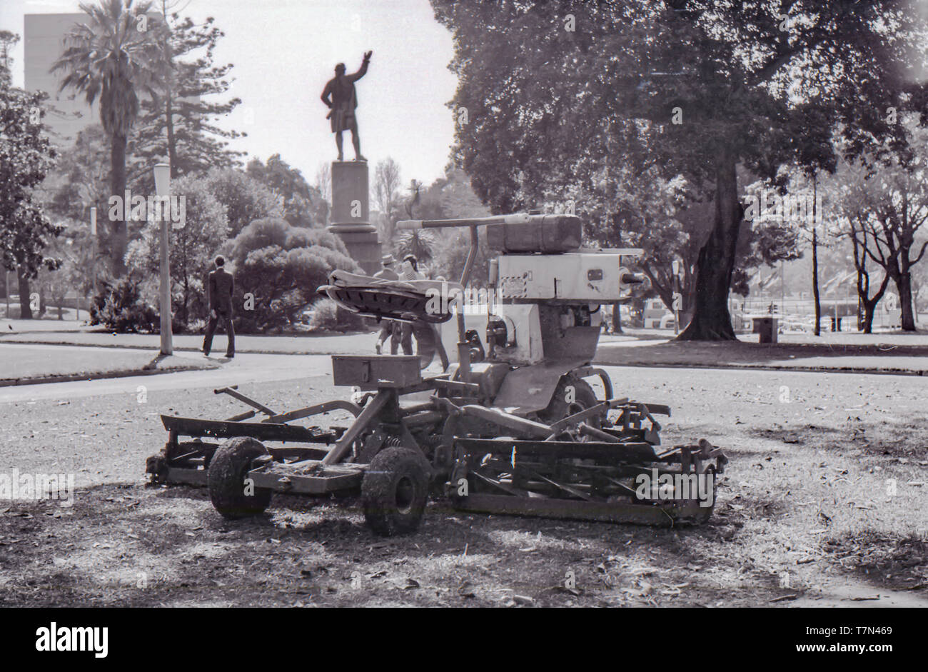 1977 Sydney Australie : UN 1970 tondeuse à siège motorisé sans surveillance sur un espace de pelouse à Sydney située au centre de la ville de Hyde Park. Dans l'arrière-plan des gens marcher le long des allées pavées et la statue du capitaine Cook se dresse contre un ciel clair. Banque D'Images