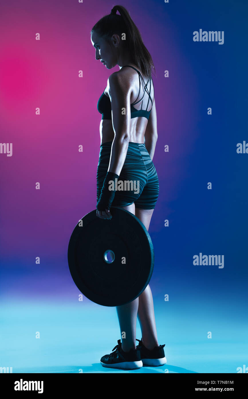 Une jeune femme tenant une plaque de poids. Athlète féminin de l'exercice avec des poids sur l'arrière-plan de couleur. Banque D'Images