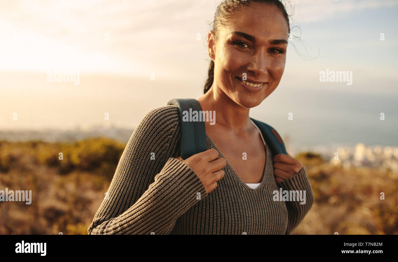 Happy woman carrying a bag marche à travers champ. Jeune femme sur le pays de la randonnée, à la caméra et au sourire. Banque D'Images