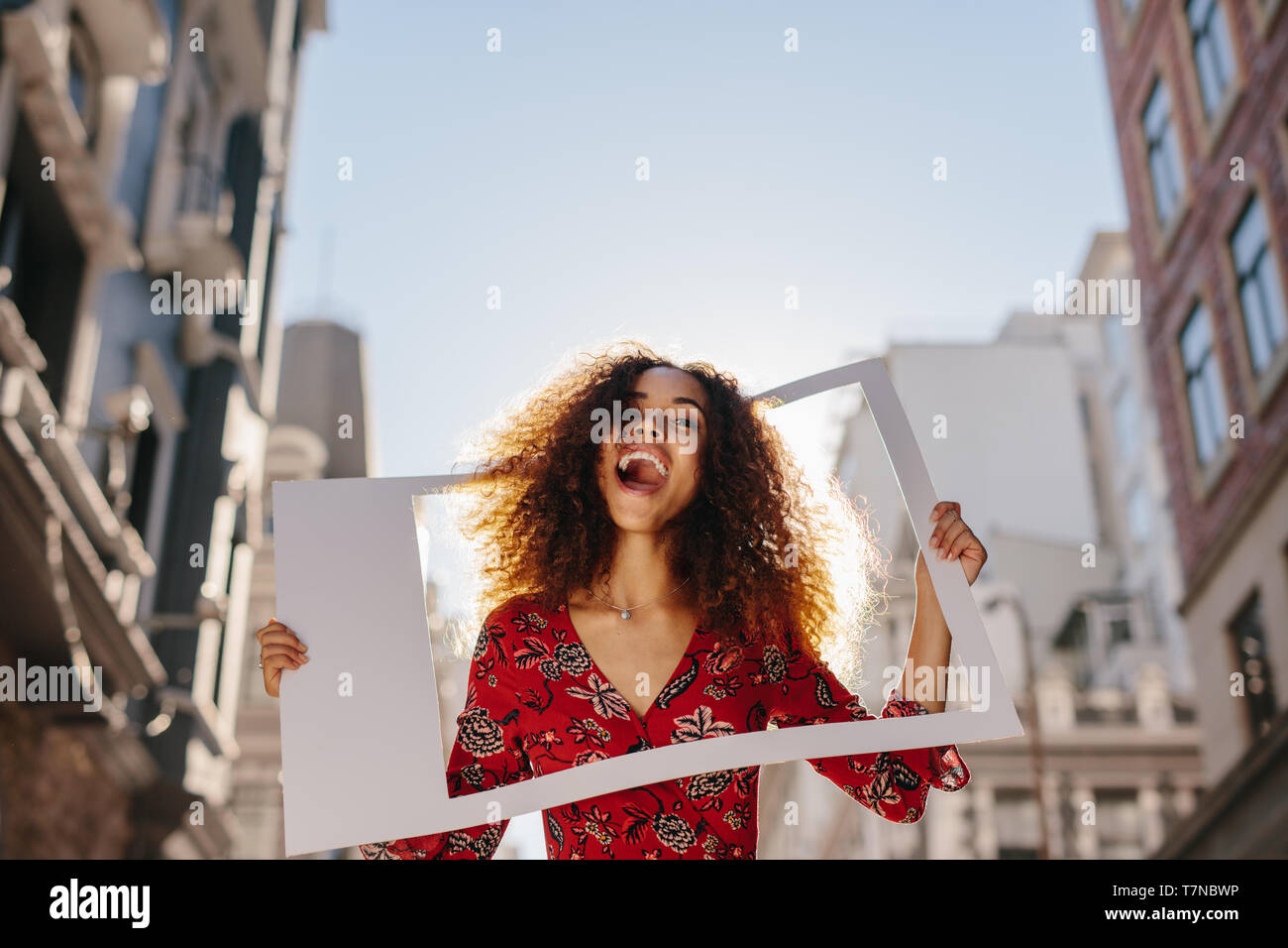 Jeune femme excité avec cadre photo vide. Les femmes traveler standing en plein air dans la ville. Banque D'Images