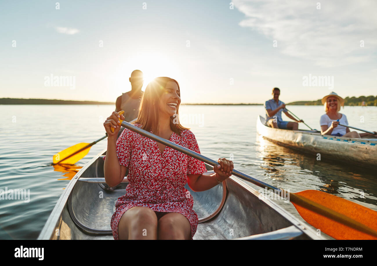 Jeune femme ayant l'amusement tout en canoë avec son petit ami et ses amis sur un lac sous le soleil d'après-midi d'été Banque D'Images