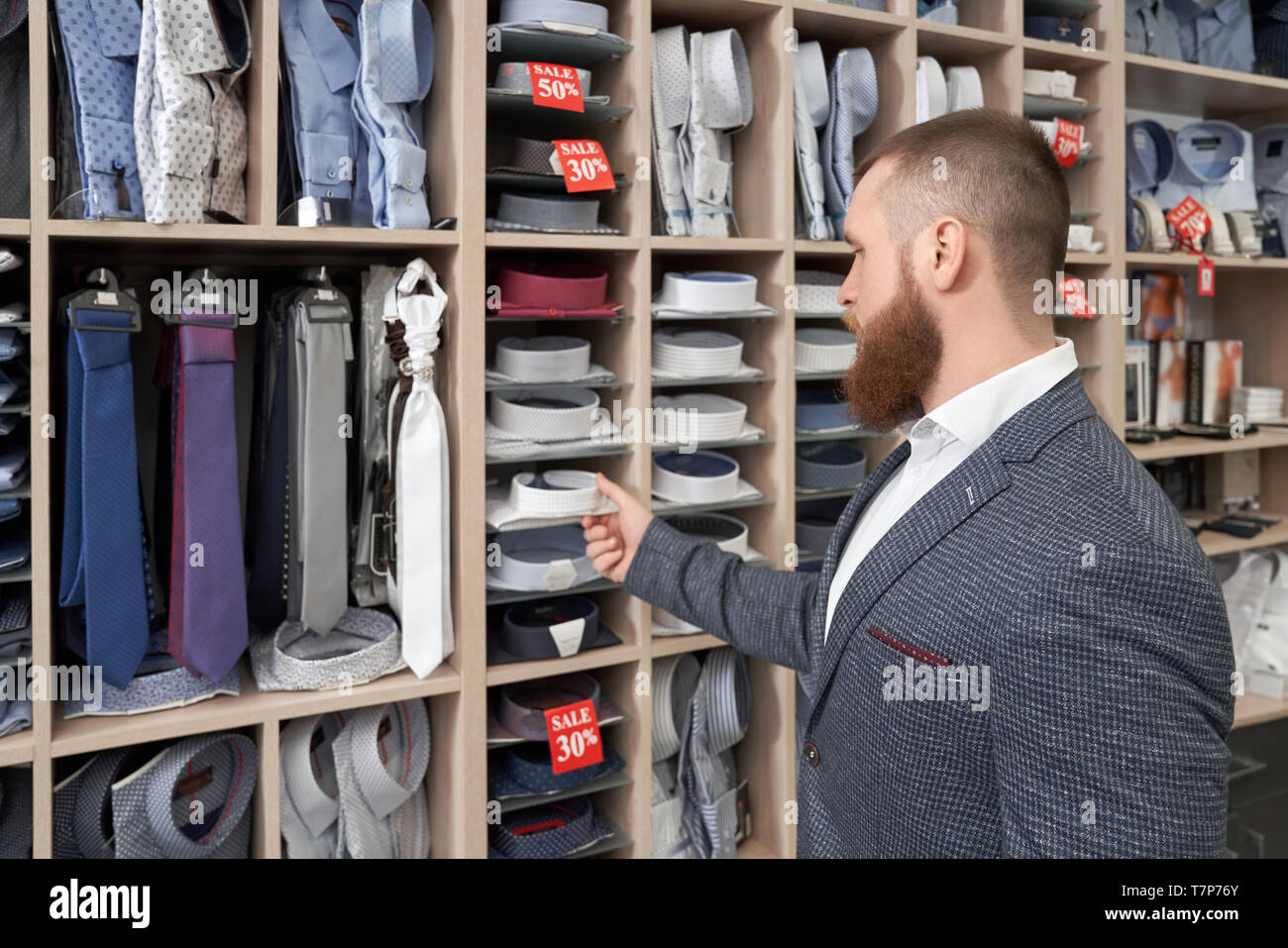 Vue de l'arrière du client mâle barbu debout près de racks avec des  vêtements et choisir nouveau maillot dans la boutique. Jeune homme portant à  la veste grise à cravates et chemise