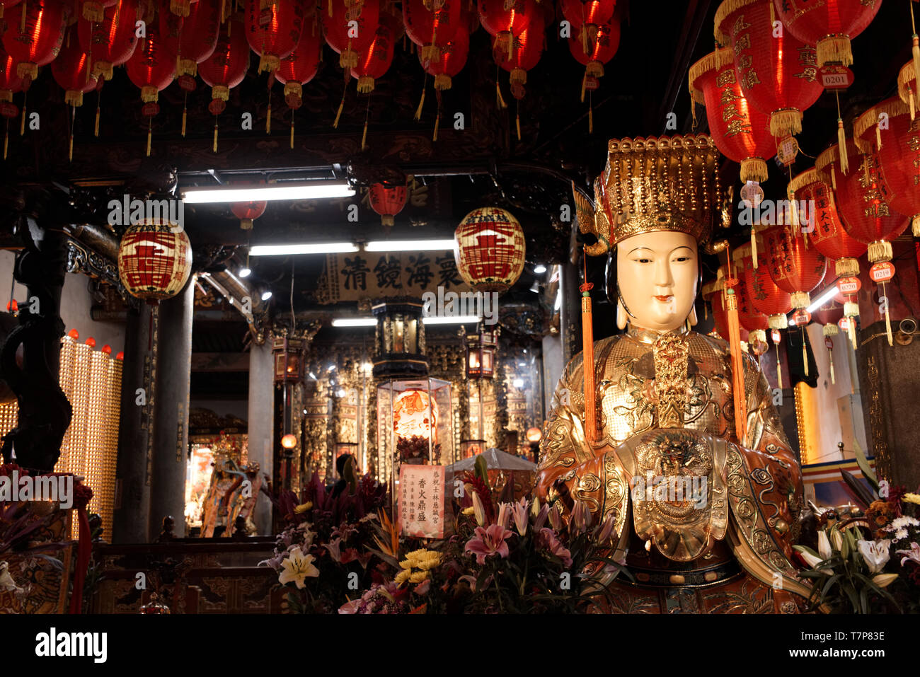 Une statue sacrée dans un temple asiatique entre lampions rouges et de fleurs Banque D'Images