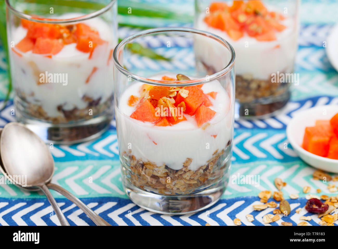 Dessert avec la papaye, le yogourt et granola dans des verres. Fond textile bleu. Banque D'Images