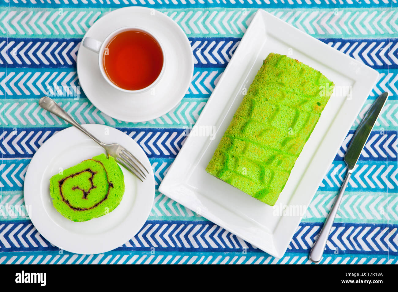 Rouleau vert gâteau avec une tasse de thé bleu sur fond textile. Vue d'en haut. Banque D'Images