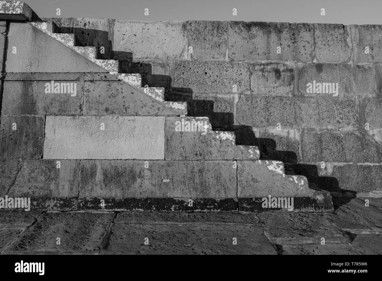 Vieux escaliers de pierre sur la Lyme Regis Cobb, tourné en noir et blanc avec des ombres contre le mur de pierre. Banque D'Images