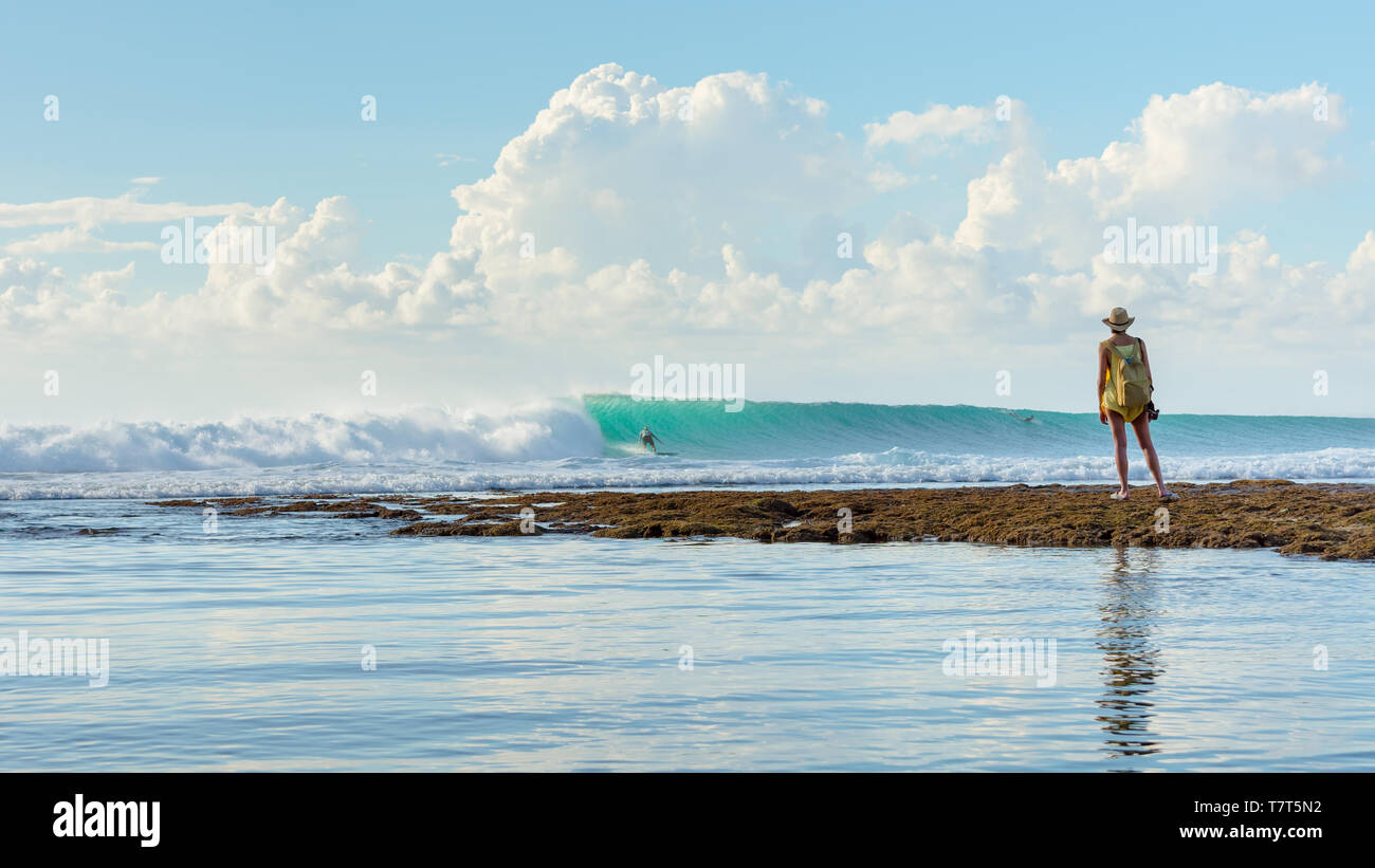 5 mai 2019 : plage de Balangan, Bali, Indonésie - une femme regardant en tant que surfer rides une belle vague avec soleil de l'après-midi l'éclairage de scène. Banque D'Images