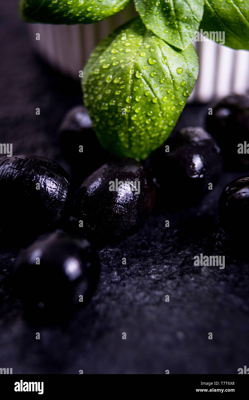 Les feuilles de basilic et olives noires sur noir table de pierre Banque D'Images