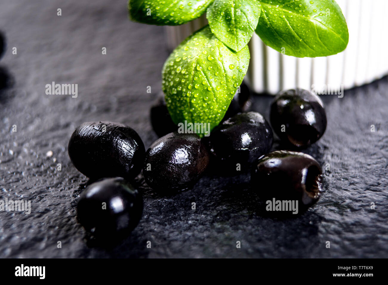 Les feuilles de basilic et olives noires sur noir table de pierre Banque D'Images