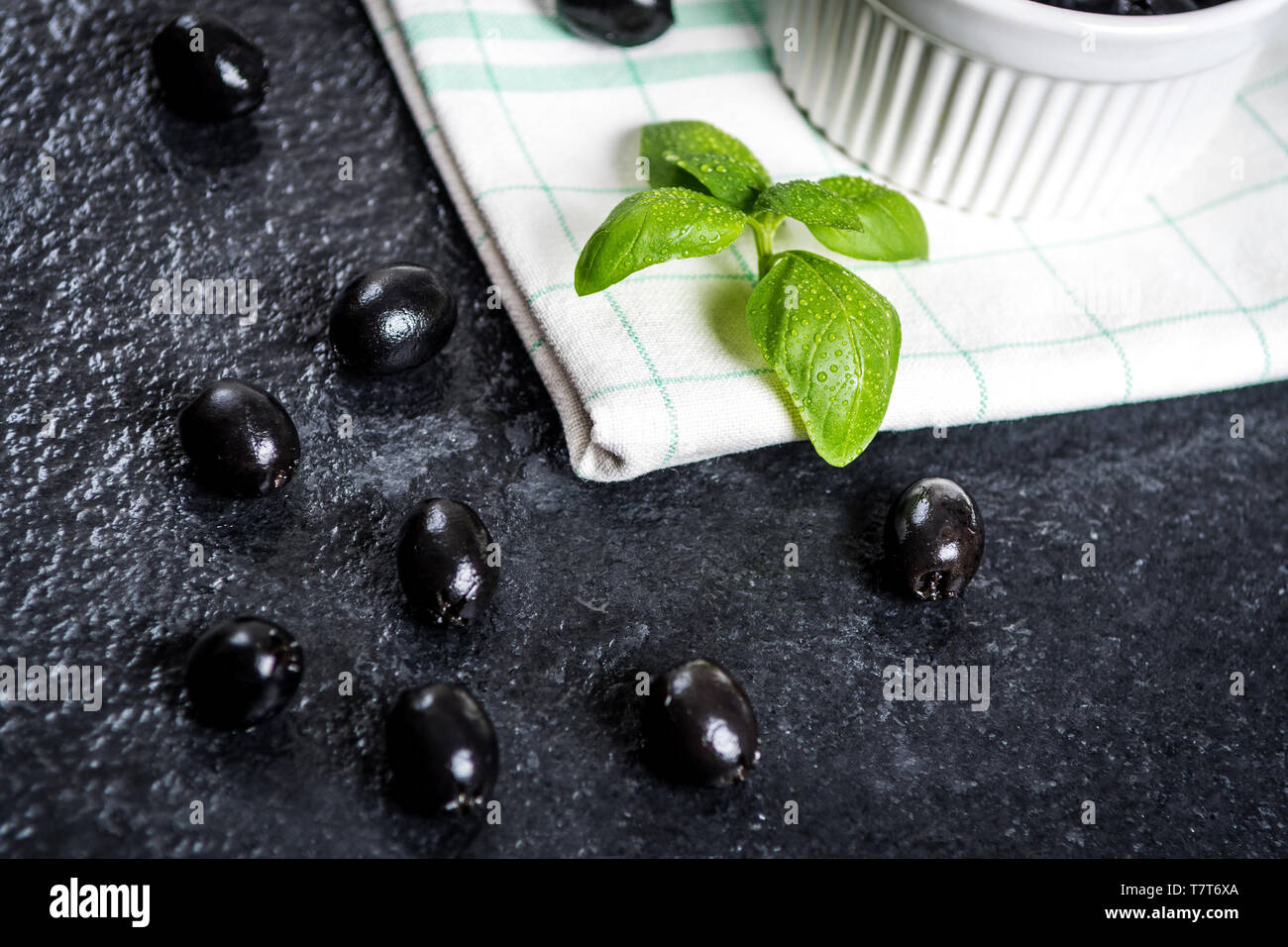 Les feuilles de basilic et olives noires sur noir table de pierre Banque D'Images