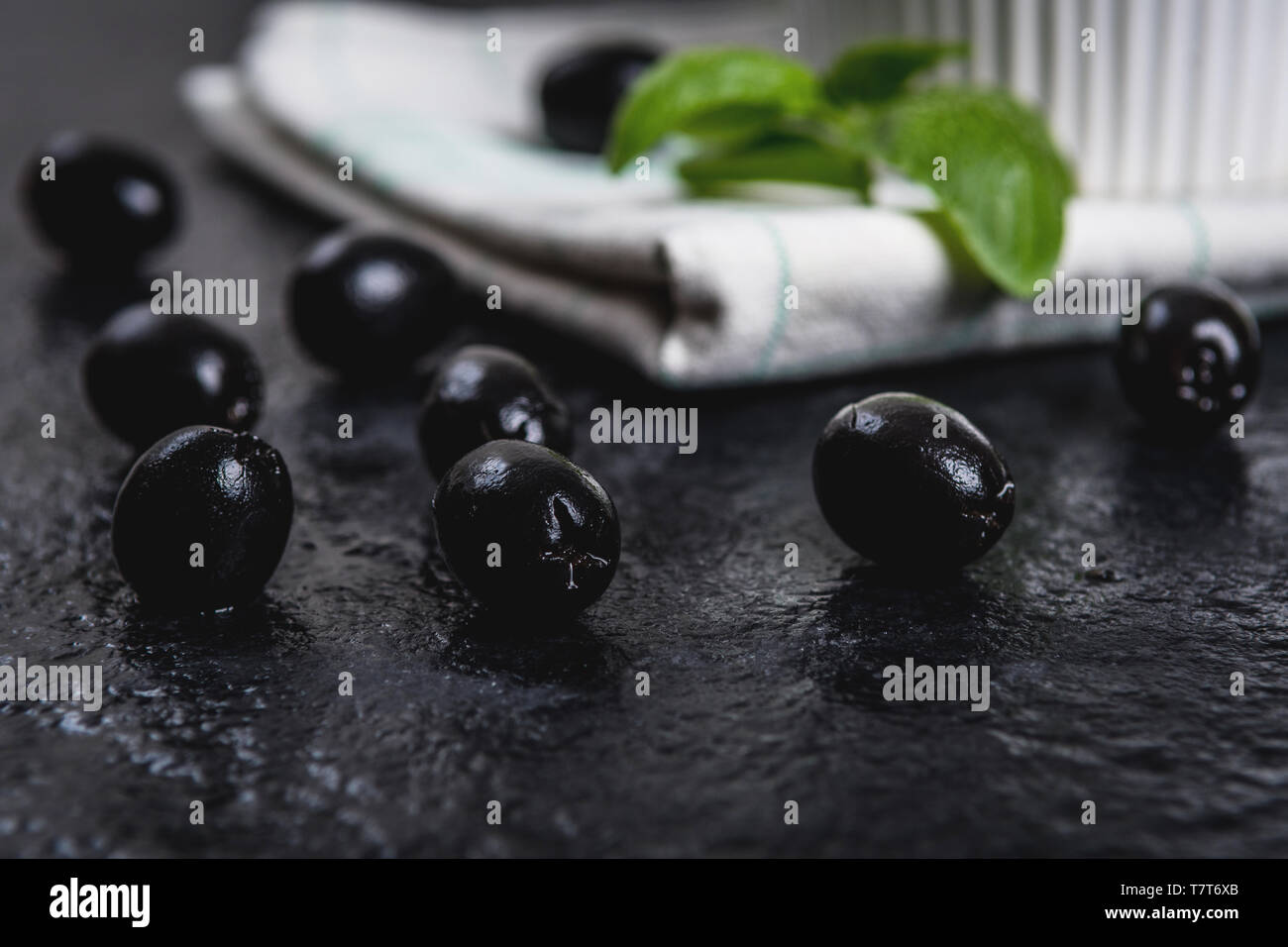 Les feuilles de basilic et olives noires sur noir table de pierre Banque D'Images