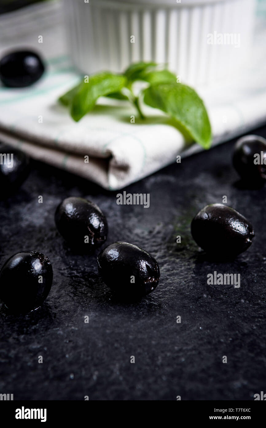 Les feuilles de basilic et olives noires sur noir table de pierre Banque D'Images