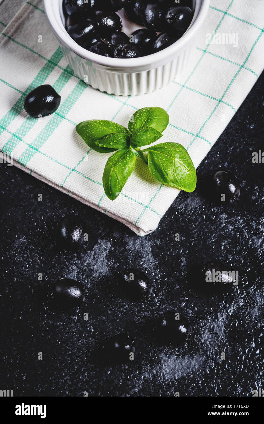 Les feuilles de basilic et olives noires sur noir table de pierre Banque D'Images