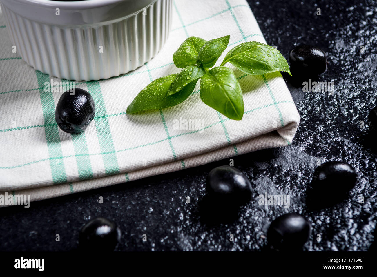 Les feuilles de basilic et olives noires sur noir table de pierre Banque D'Images