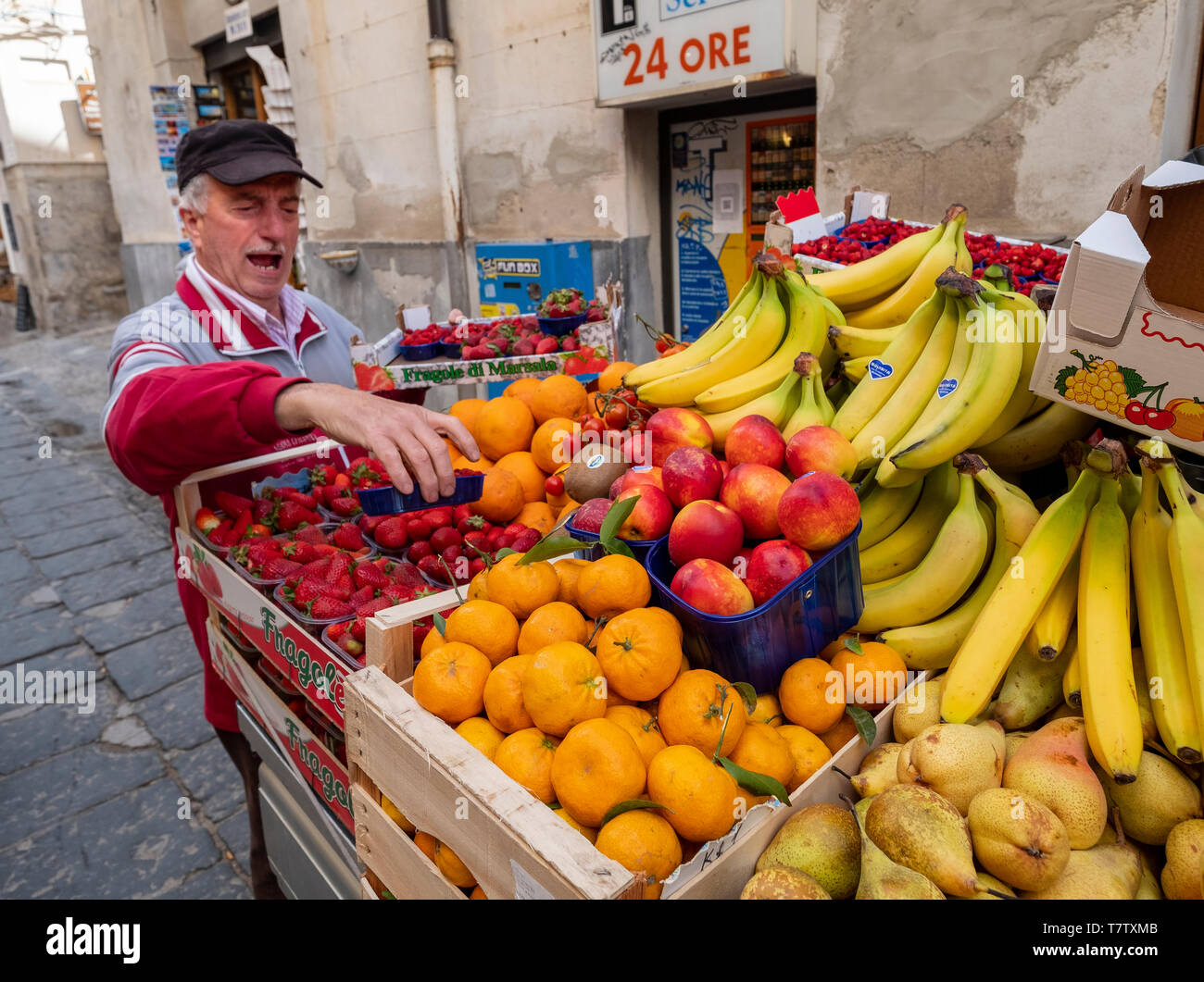 Un homme vend des fruits sur une rue latérale à Cefalu en Sicile. Banque D'Images