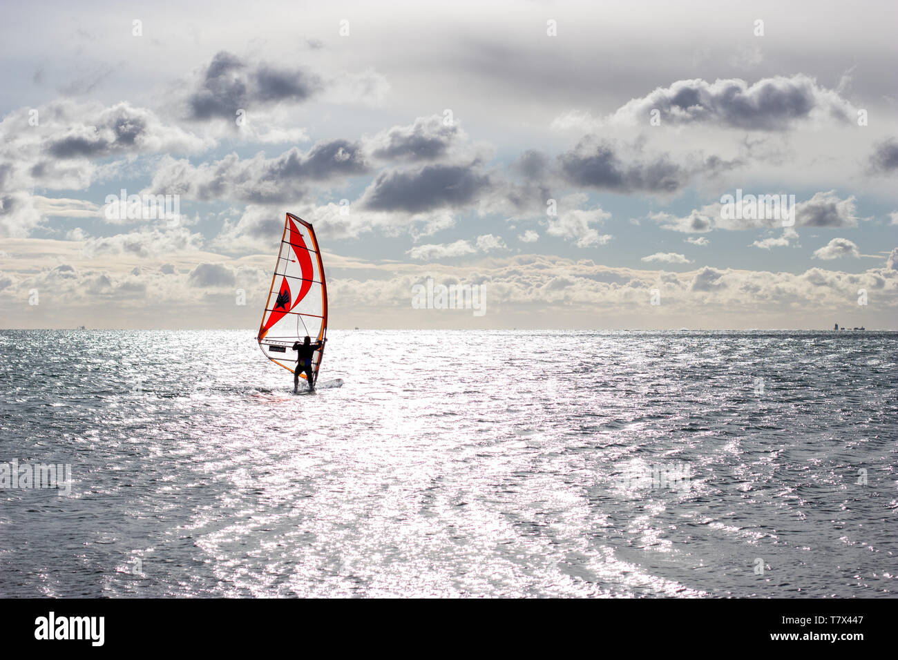 Un surfeur de vent solitaire naviguant sur une mer calme avec une voile rouge par une journée ensoleillée Banque D'Images