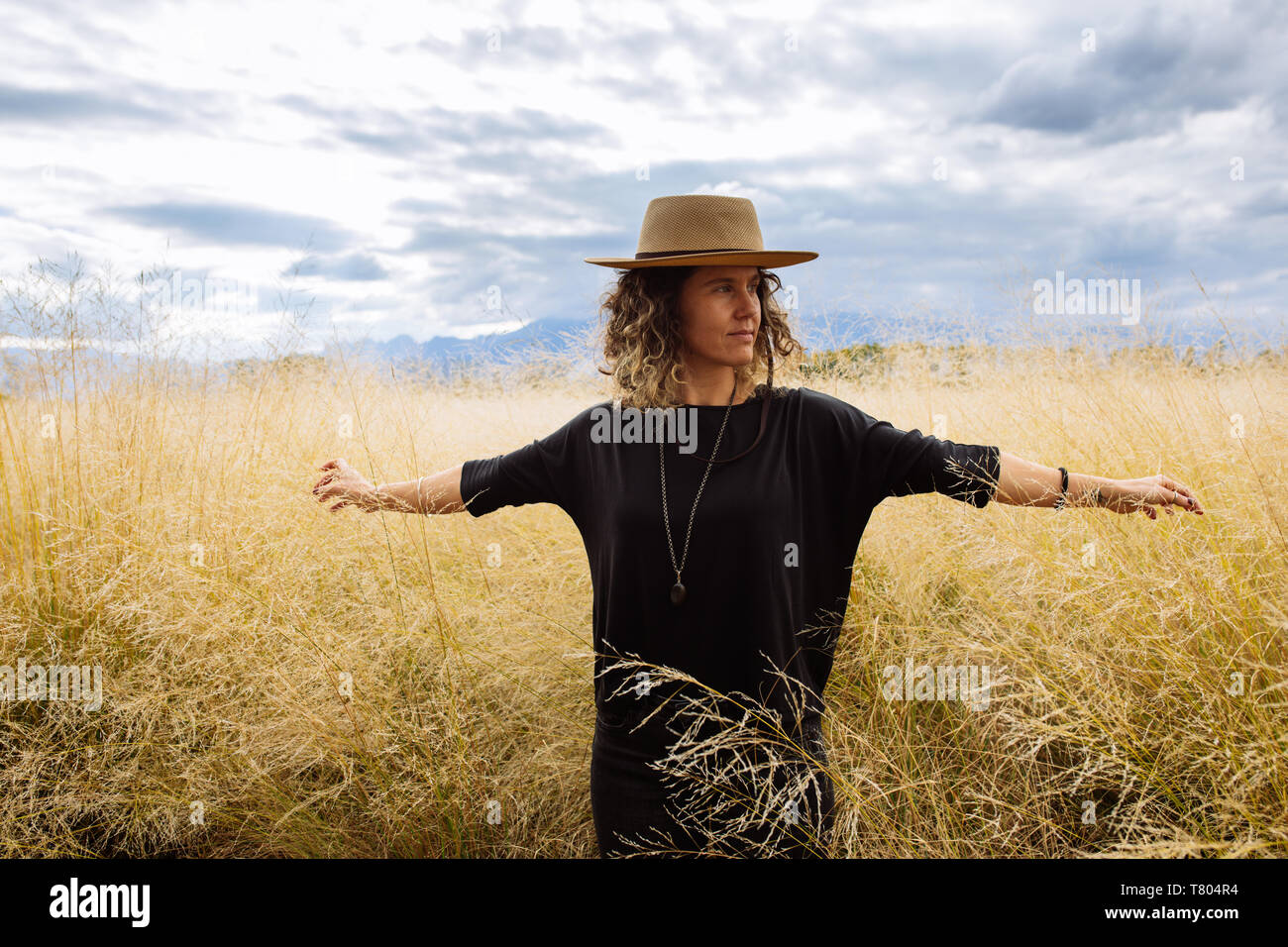 Femme dans la mi-trentaine, posant à bras ouverts avec un chapeau dans un champ d'herbe jaune dans Bodega Septima Winery à Mendoza, Argentine Banque D'Images