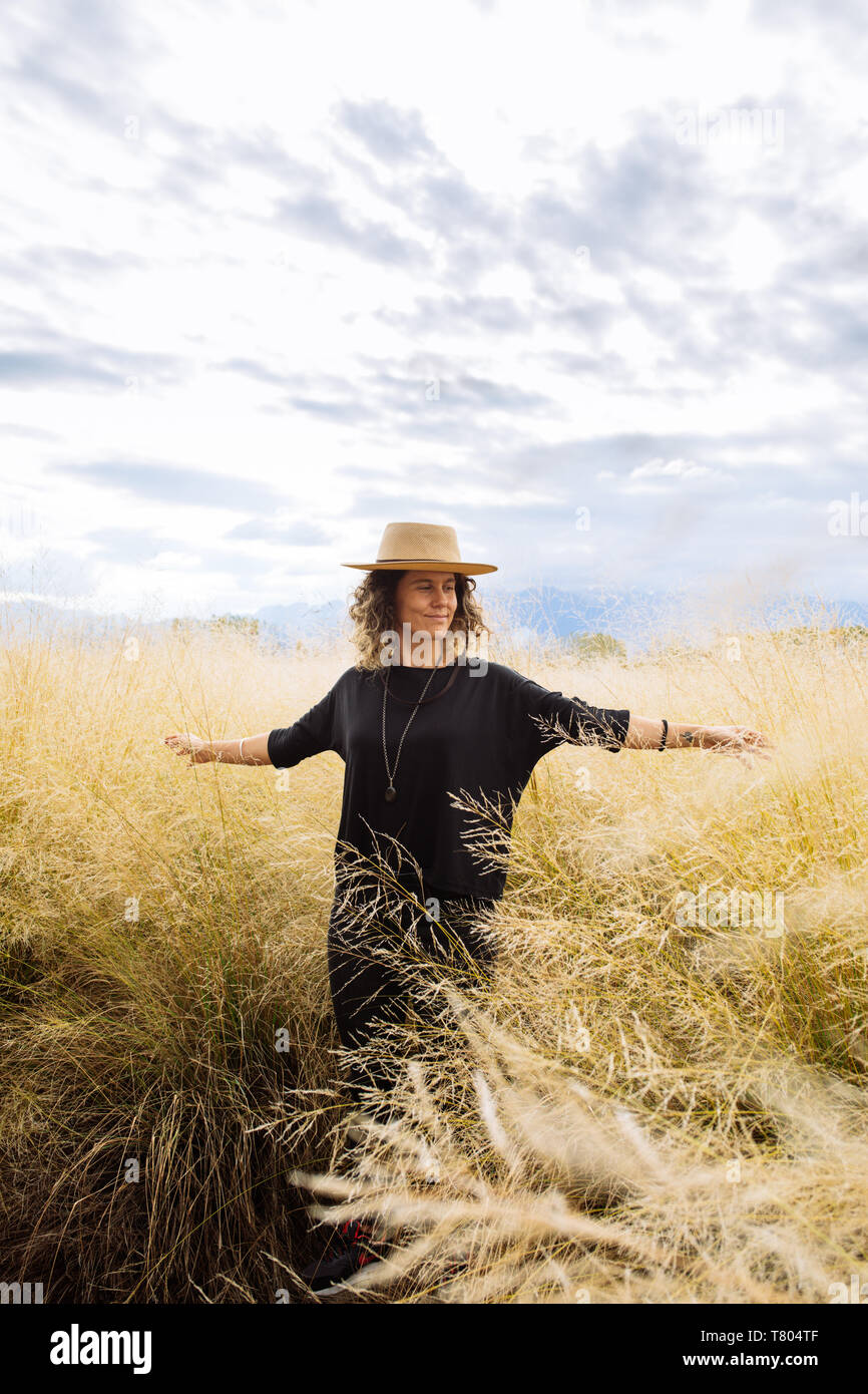 Femme dans la mi-trentaine, posant à bras ouverts avec un chapeau dans un champ d'herbe jaune dans Bodega Septima Winery à Mendoza, Argentine Banque D'Images