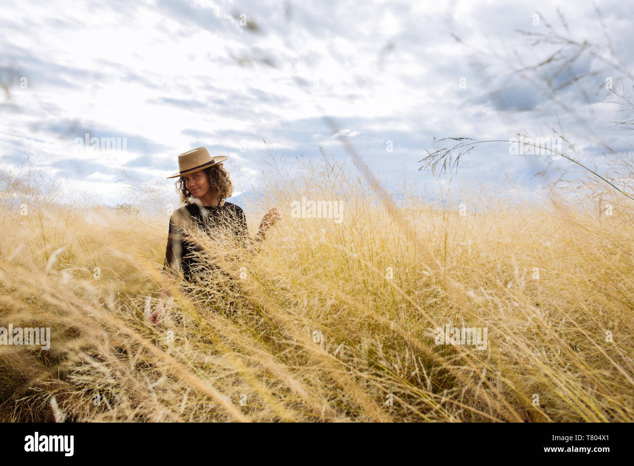 Femme dans la mi-trentaine, la marche dans la longue herbe jaune avec un chapeau dans un champ en Bodega Septima Winery à Mendoza, Argentine Banque D'Images