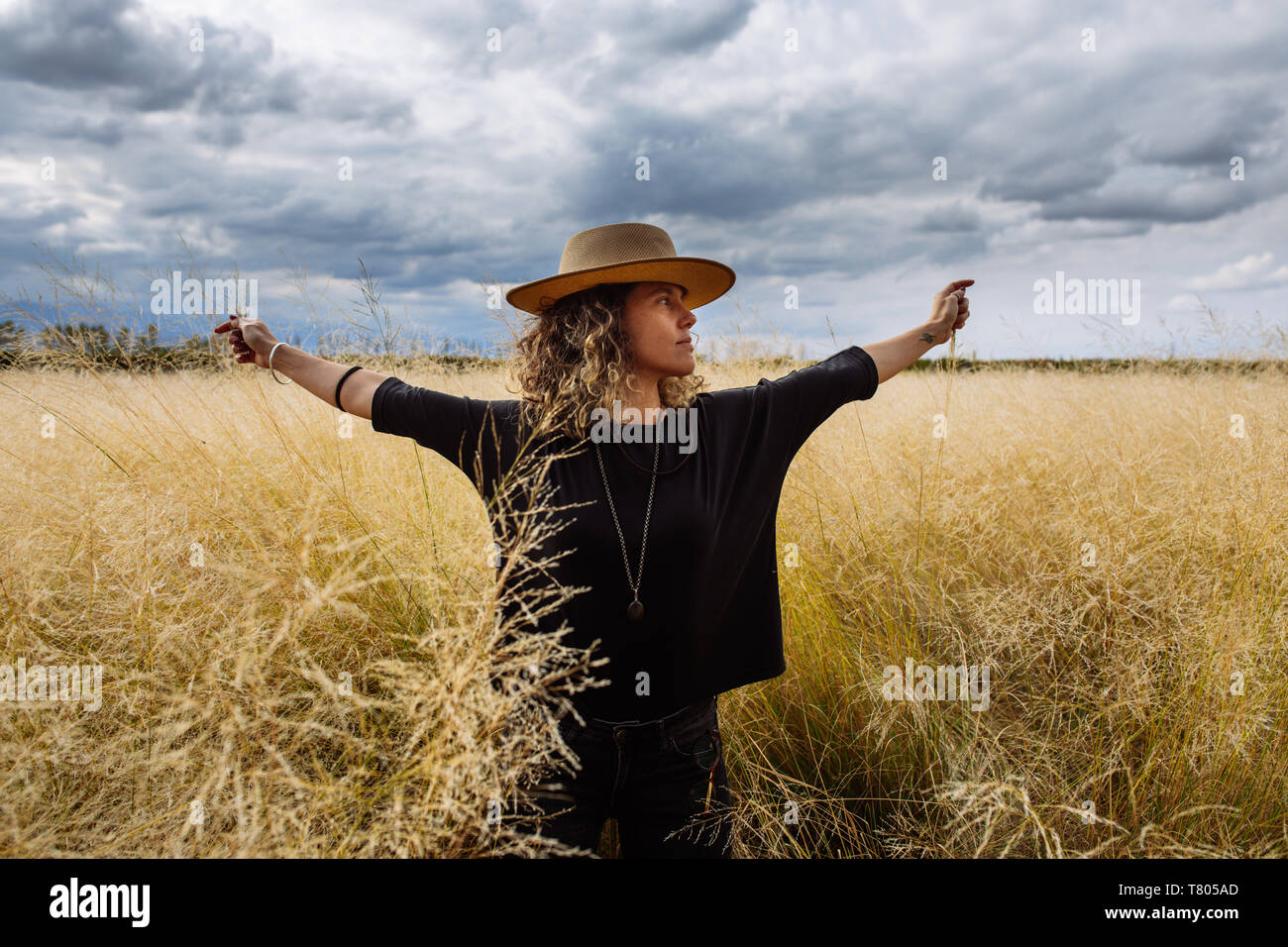Femme dans la mi-trentaine, posant à bras ouverts avec un chapeau dans un champ d'herbe jaune dans Bodega Septima Winery à Mendoza, Argentine Banque D'Images