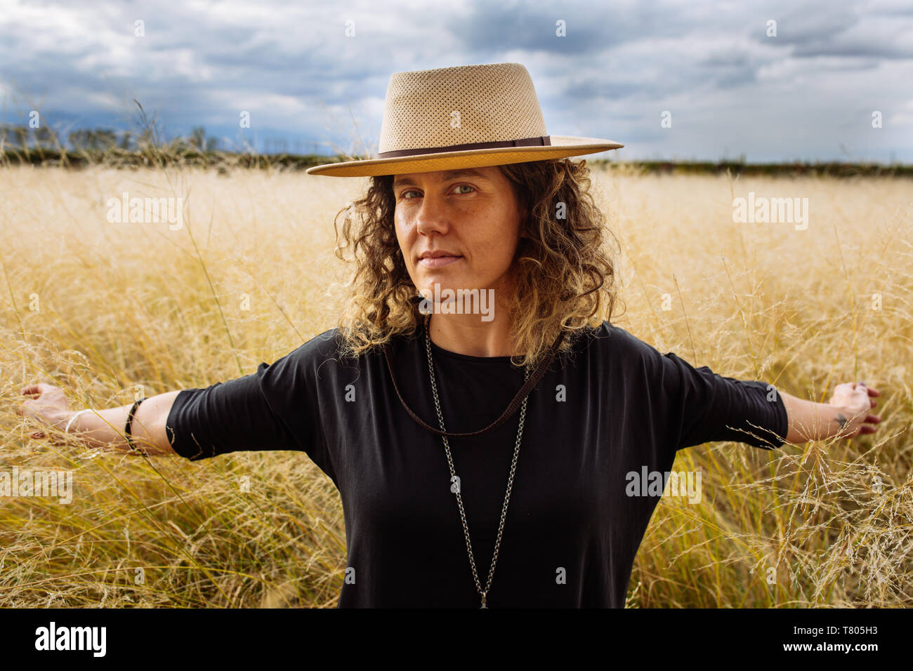 Femme dans la mi-trentaine, posant à bras ouverts avec un chapeau dans un champ d'herbe jaune dans Bodega Septima Winery à Mendoza, Argentine Banque D'Images