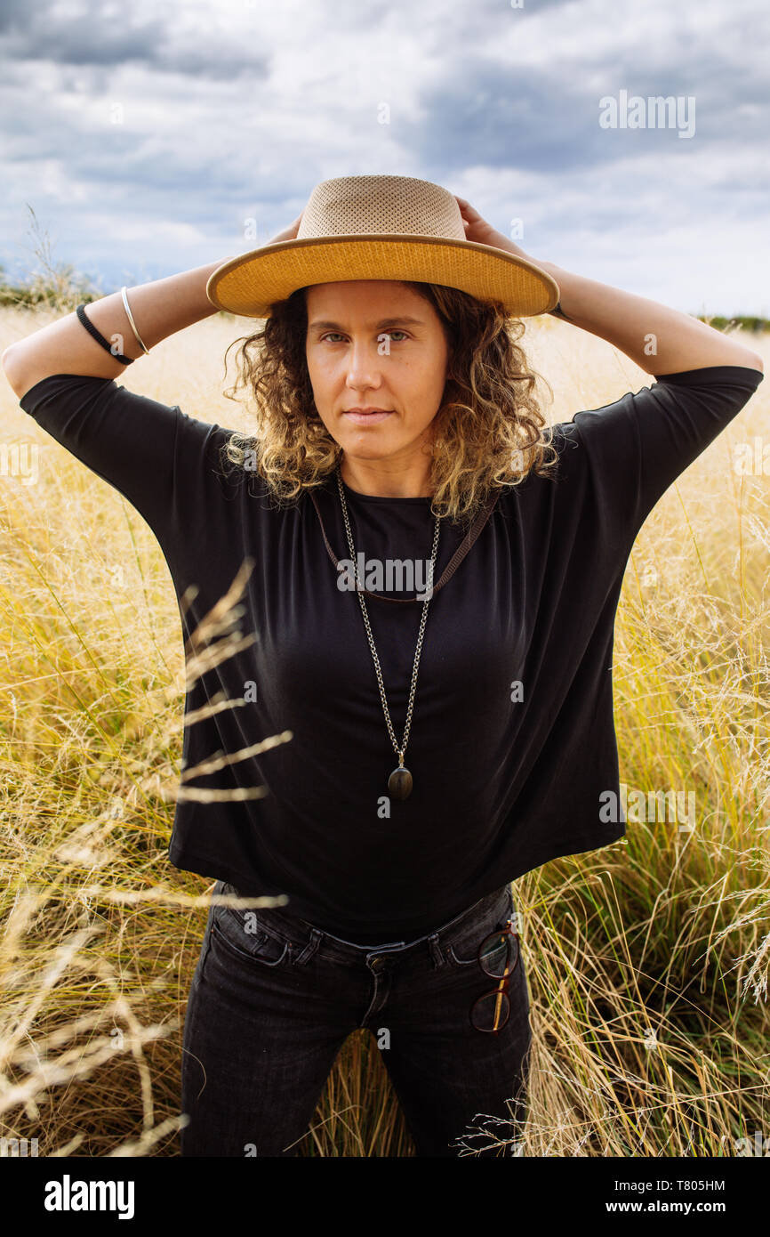 Femme dans la mi-trentaine, posant avec un chapeau dans un champ d'herbe jaune dans Bodega Septima Winery à Mendoza, Argentine Banque D'Images