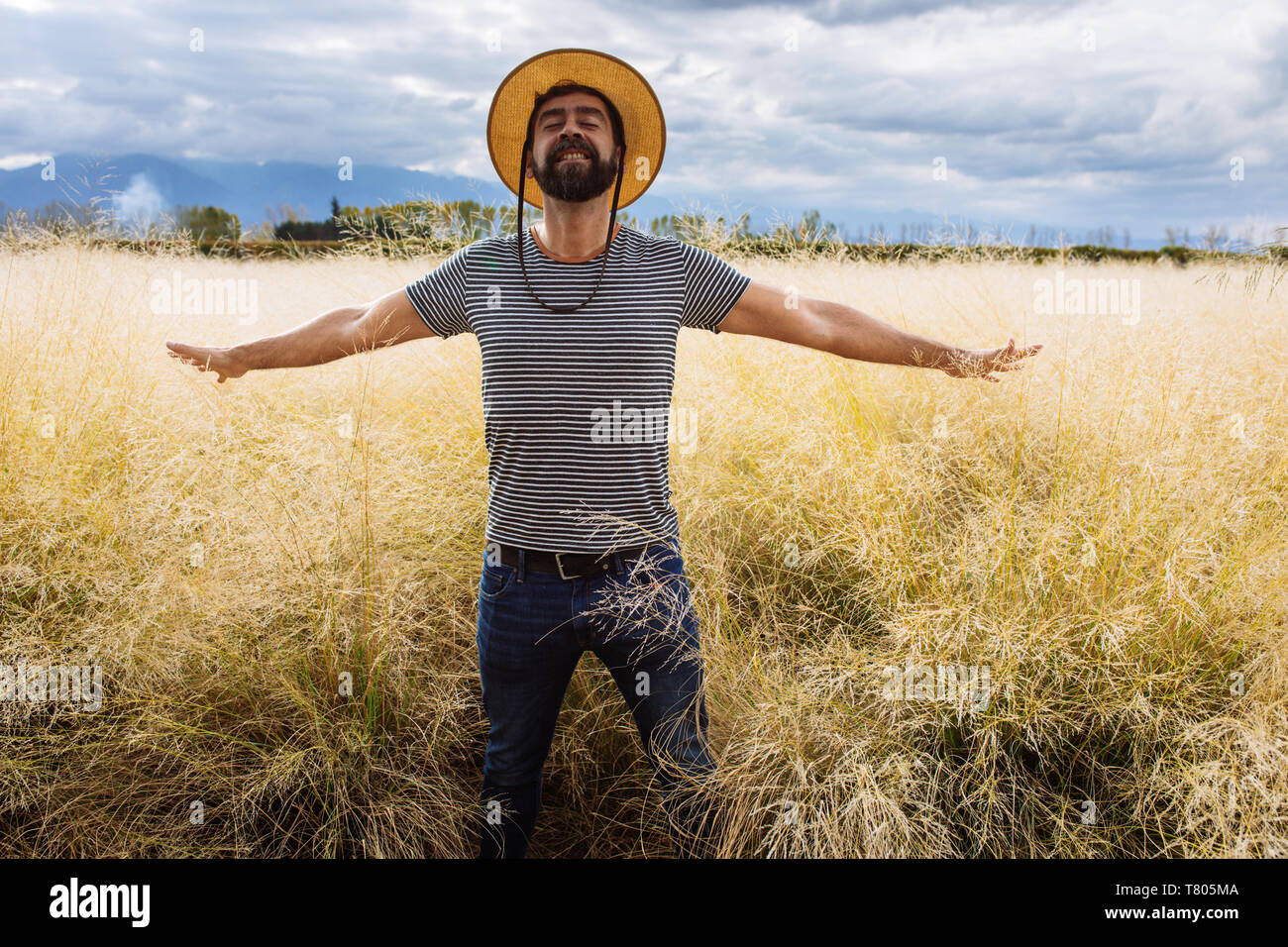 L'homme dans sa fin des années trente la mi-mi quarantaine, qui posent avec les bras ouverts et les yeux fermés dans un champ d'herbe jaune dans Bodega Septima Winery à Mendoza, Argentine Banque D'Images