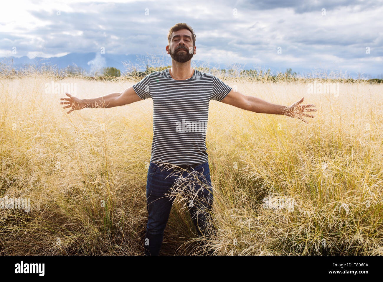 L'homme dans sa fin des années trente la mi-mi quarantaine, qui posent avec les bras ouverts et les yeux fermés dans un champ d'herbe jaune dans Bodega Septima Winery à Mendoza, Argentine Banque D'Images