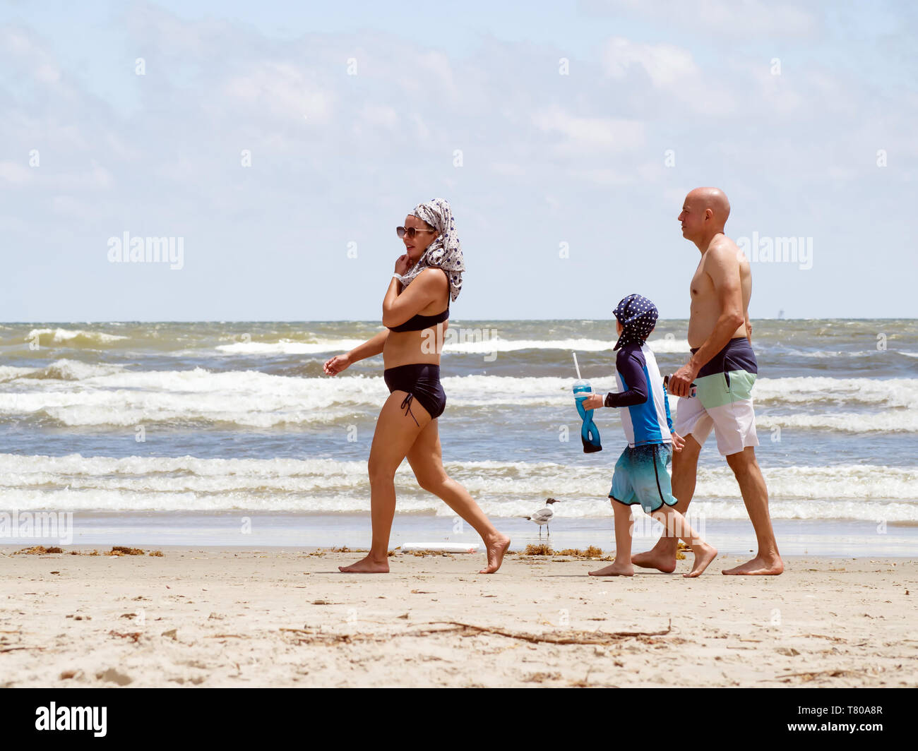 Une femme portant un maillot de bain deux pièces et hijab, un enfant portant  le hijab, et un homme en maillot de bain à pied sur un Port Aransas, Texas  Beach Photo