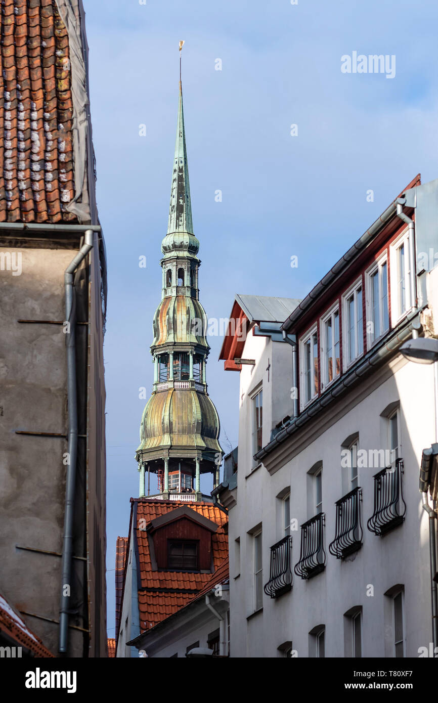 Riga. La Lettonie. La tour de Saint Peters Church peut être vu entre les anciennes maisons de Riga. Banque D'Images