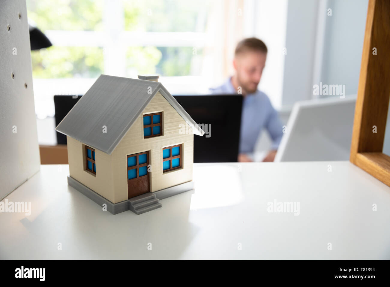 Modèle de maison sur la durée et l'homme travaillant dans l'arrière-plan au bureau Banque D'Images