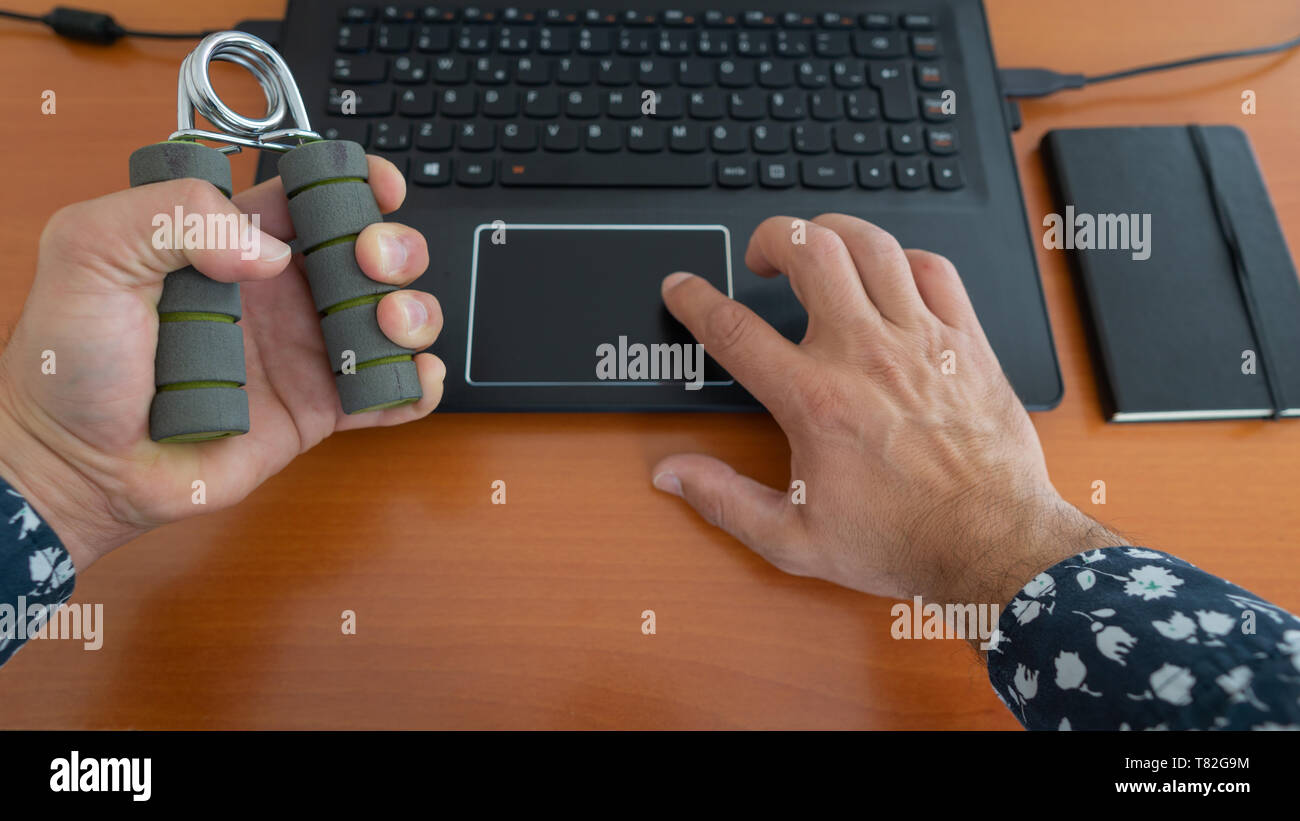 Les mains d'un homme à l'aide d'ordinateur portable et l'exercice avec le ressort-grip à Canada Place, dans son bureau de travail et l'entraînement avec.les mains en même temps. Des parties du corps. Banque D'Images