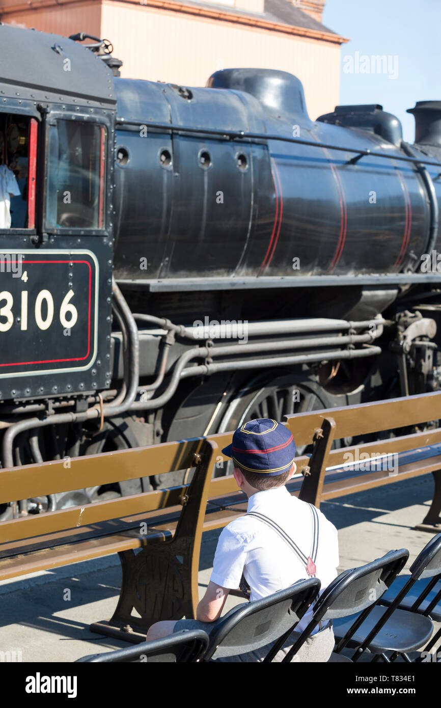 Manifestation : guerre DVS Vue arrière de 1940 school boy à cap & accolades, assis sur la plate-forme à regarder les trains à vapeur d'époque rêve de devenir conducteur de train Banque D'Images