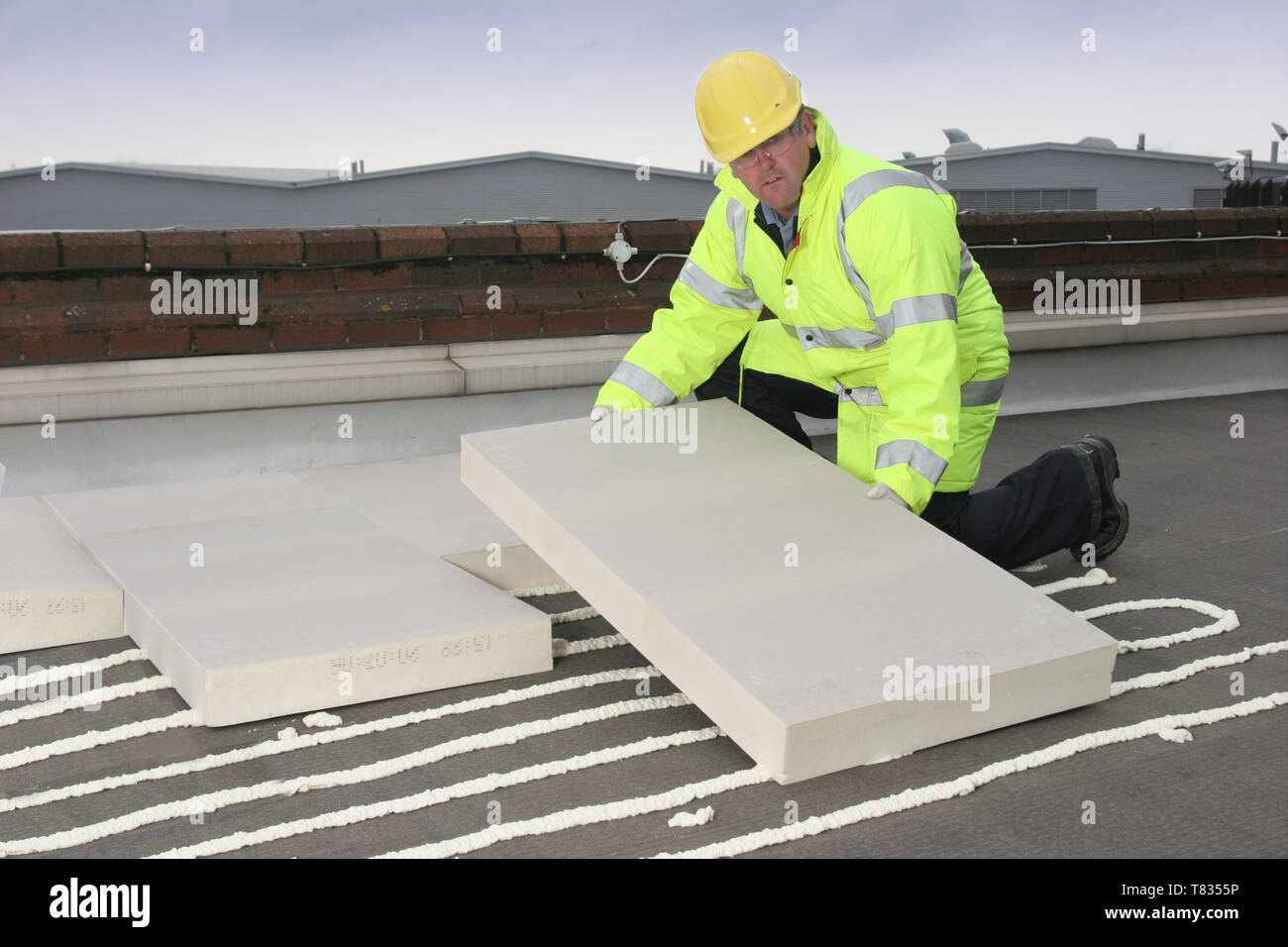 Un constructeur d'installer une isolation thermique supplémentaire sur un toit plat en plaçant des blocs sur l'isolation en mousse adhésif pulvérisé. Banque D'Images