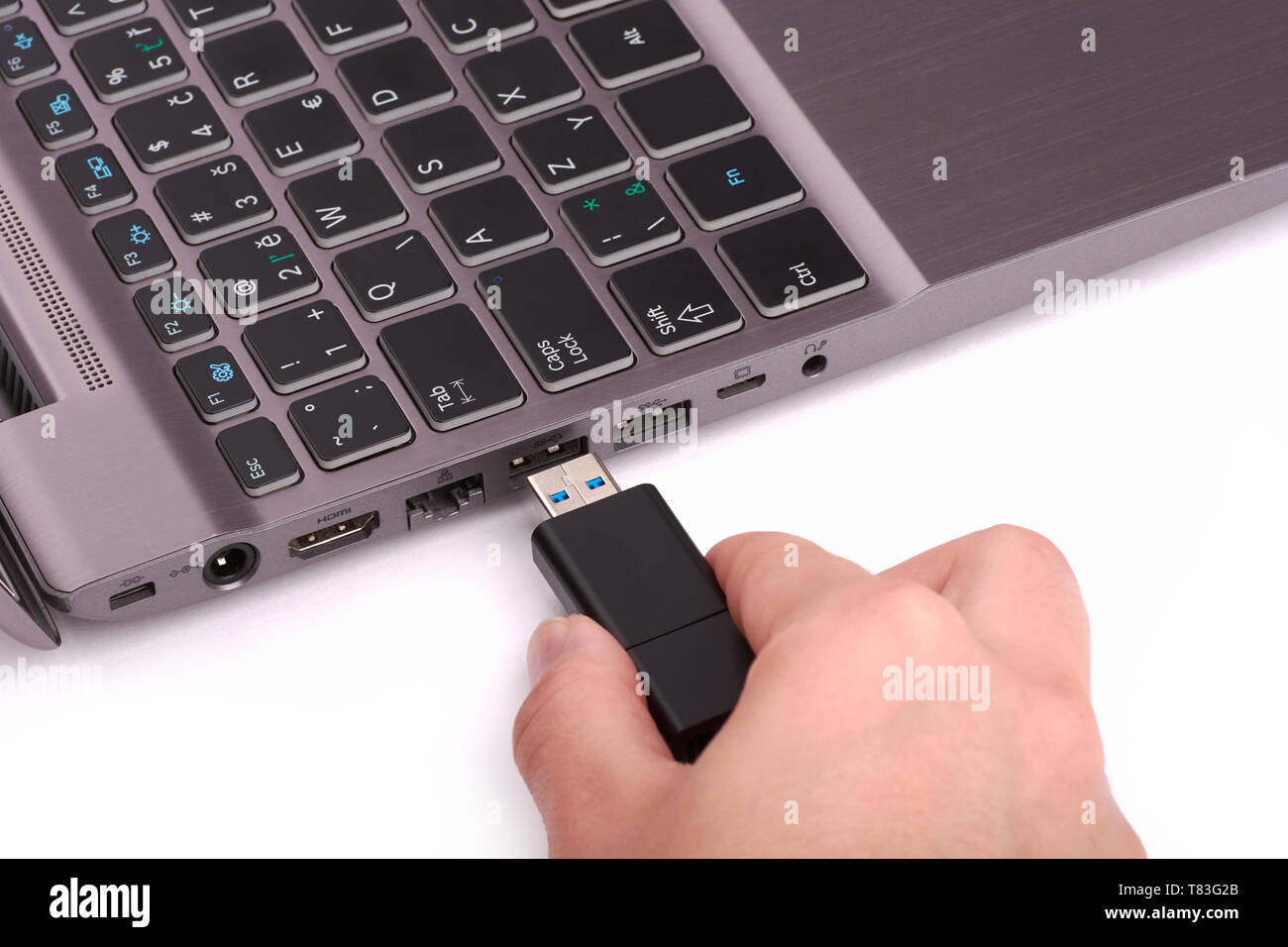 La main d'une jeune femme se connecte un lecteur flash USB à un port dans un ordinateur portable avec un clavier noir. Isolé sur fond blanc. Banque D'Images