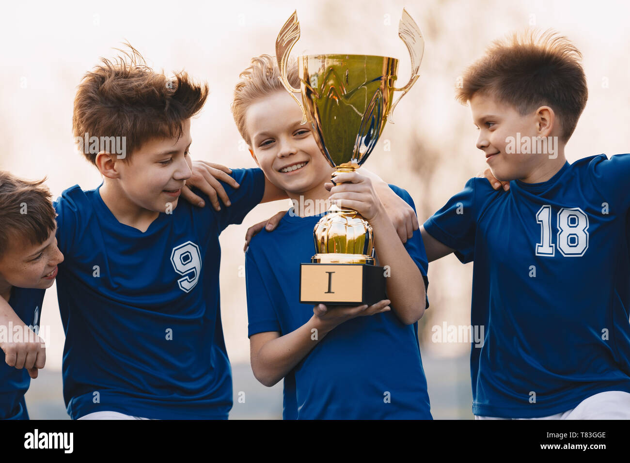 Les garçons de l'équipe sports célébrant la victoire. Des enfants heureux holding golden trophy. L'équipe de football pour enfants sensibilisation des vainqueurs de coupe. Succès sportifs pour la jeunesse Banque D'Images