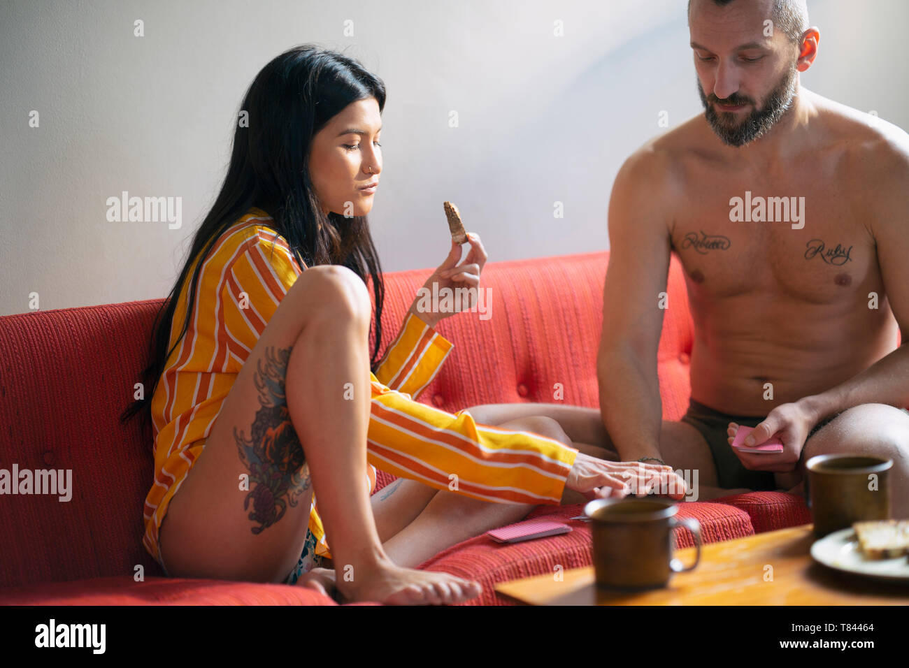 Couple Hipster cartes à jouer et de prendre le petit déjeuner sur canapé Banque D'Images