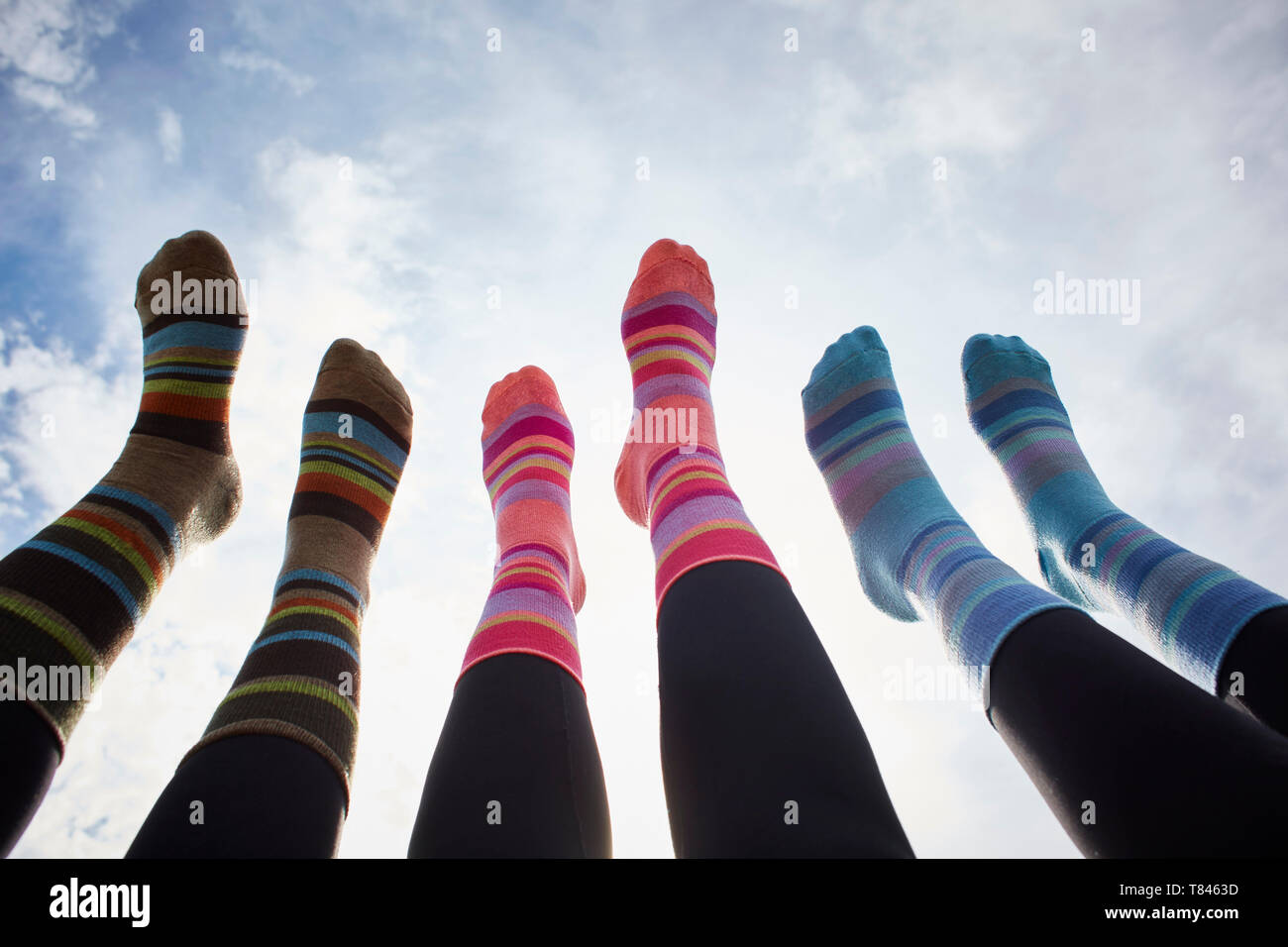 Trois jeunes femmes en chaussettes rayées avec jambes soulevées contre ciel ensoleillé, portrait de jambes Banque D'Images