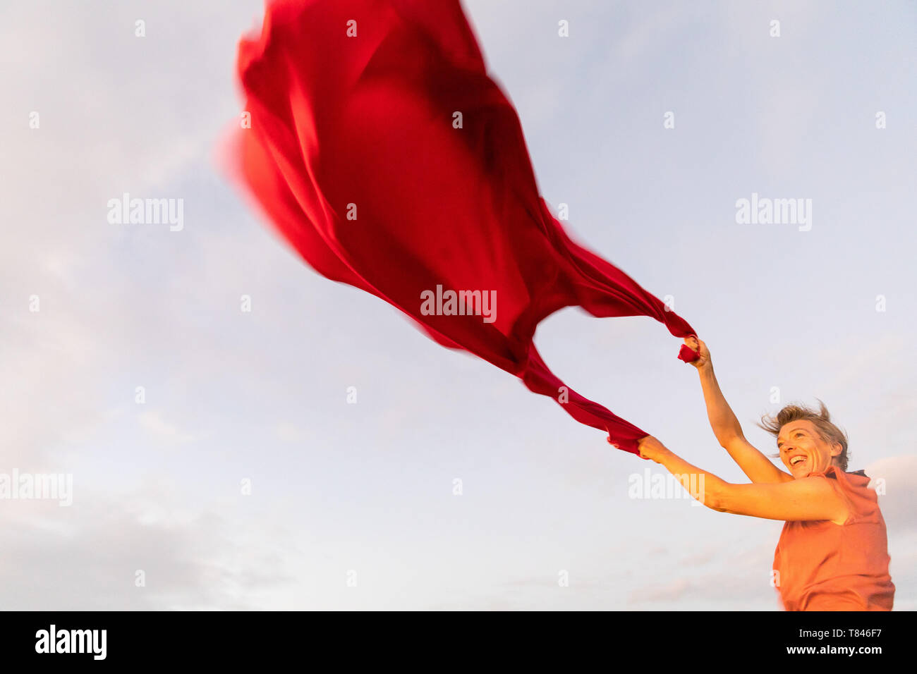 Woman holding up tissu rouge voletant dans le vent Banque D'Images