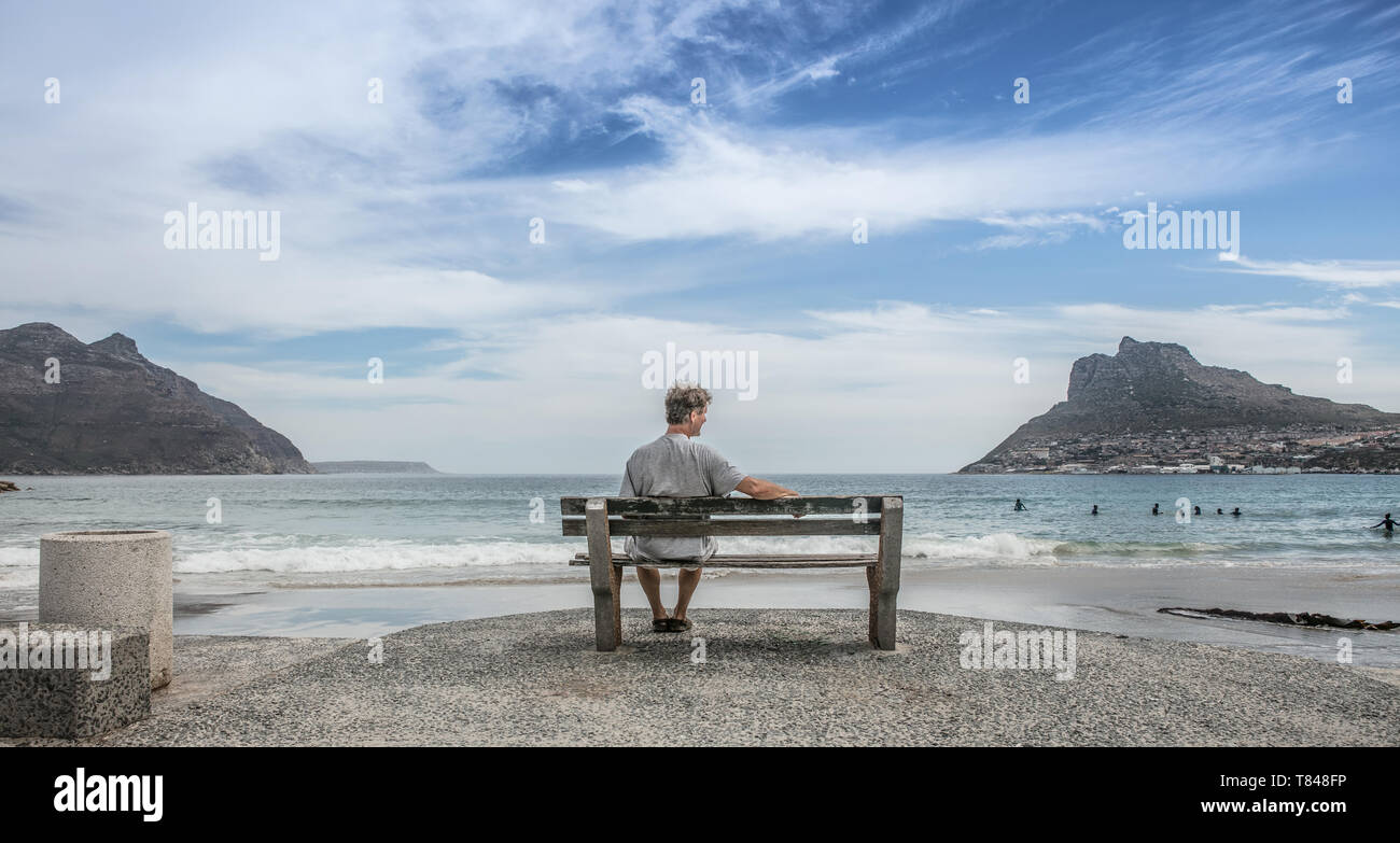 Homme mûr assis à la plage de banc, Cape Town, Western Cape, Afrique du Sud Banque D'Images