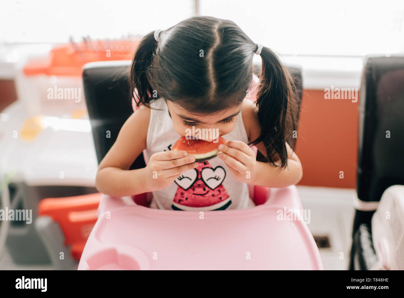 Fille dans une chaise haute manger melon d'eau Banque D'Images