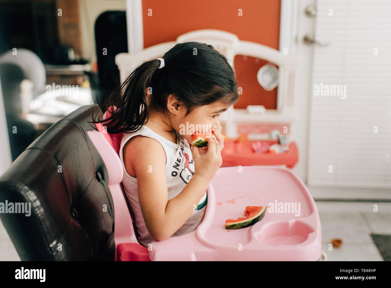 Fille dans une chaise haute de l'eau manger melon, side view Banque D'Images