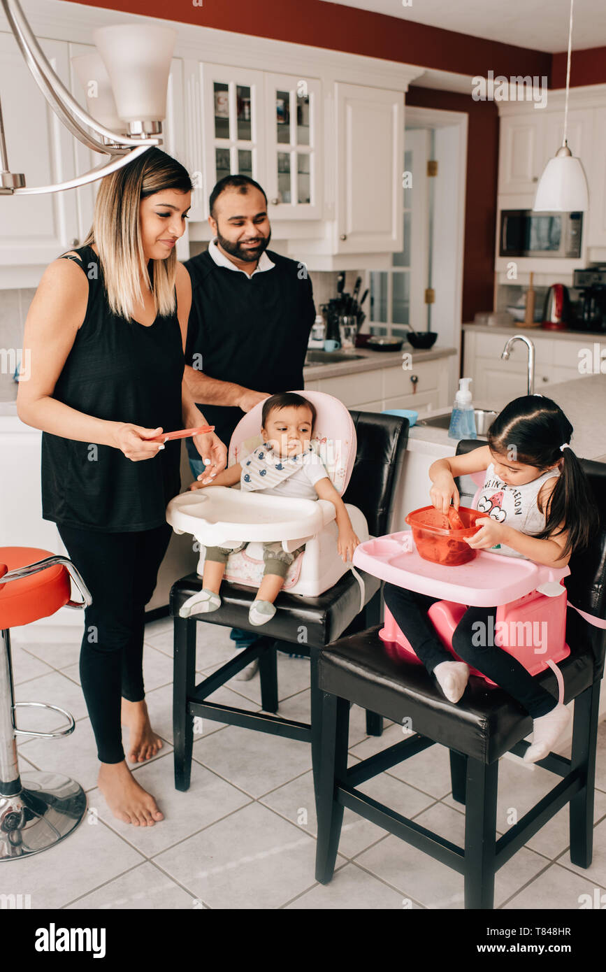 Couple dans la cuisine avec sa fille et son bébé dans des chaises hautes Banque D'Images