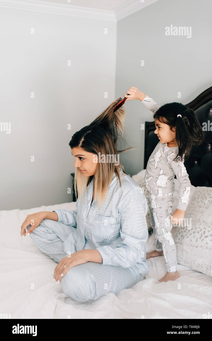 Girl brushing mother's cheveux sur lit dans la matin Banque D'Images