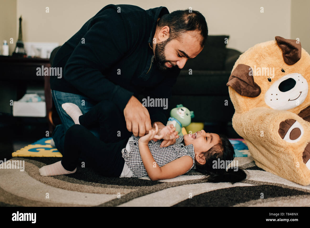 Le père de sa fille chatouillant sur plancher du salon Banque D'Images