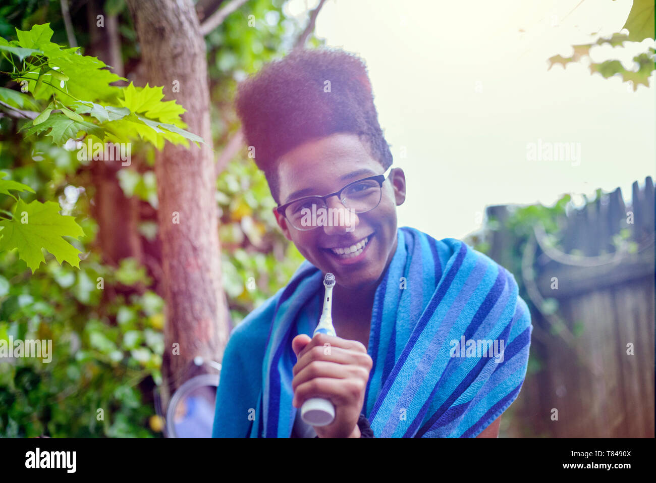 Teenage boy avec dessus plat afro hairstyle holding brosse à dents électrique dans la région de jardin, portrait Banque D'Images