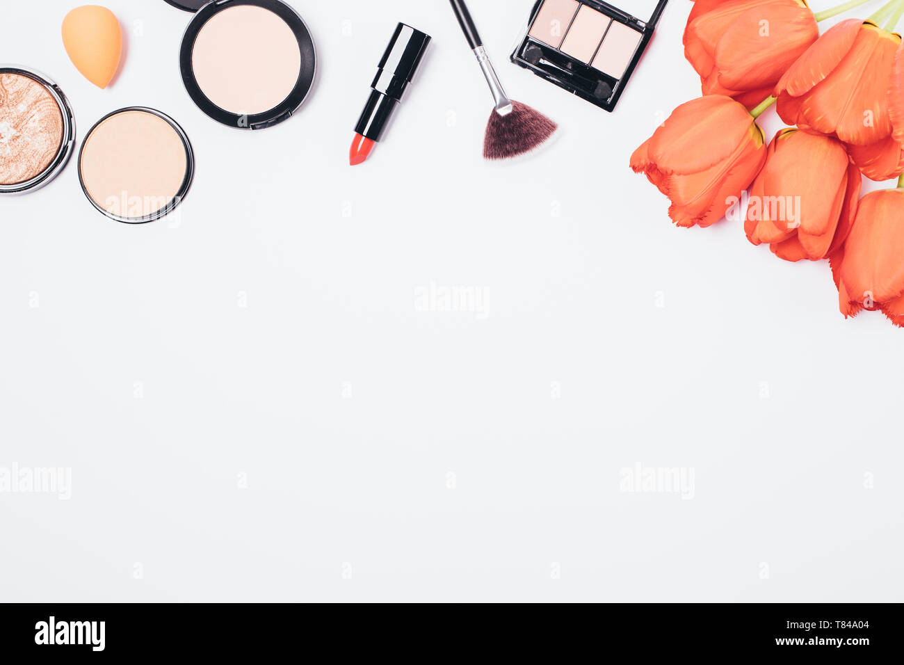 Arrière-plan de maquillage rouges à lèvres, poudres et pinceaux avec bouquet de fleurs sur le tableau blanc avec copie espace télévision, jeter l'arrangement. Banque D'Images
