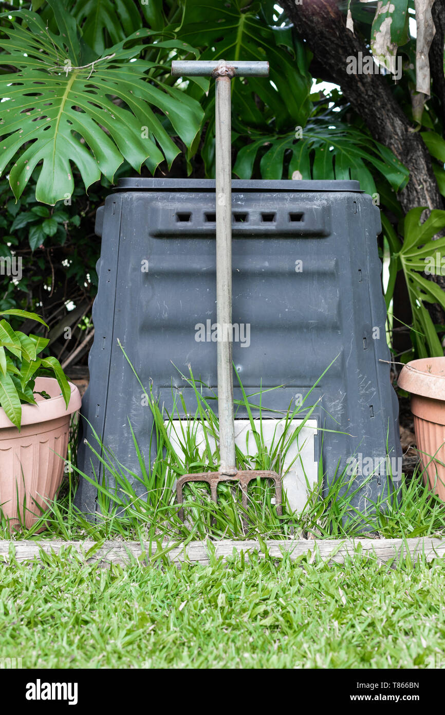 Un composteur et fourche dans un jardin à l'arrière, entouré par les plantes et l'herbe verte Banque D'Images