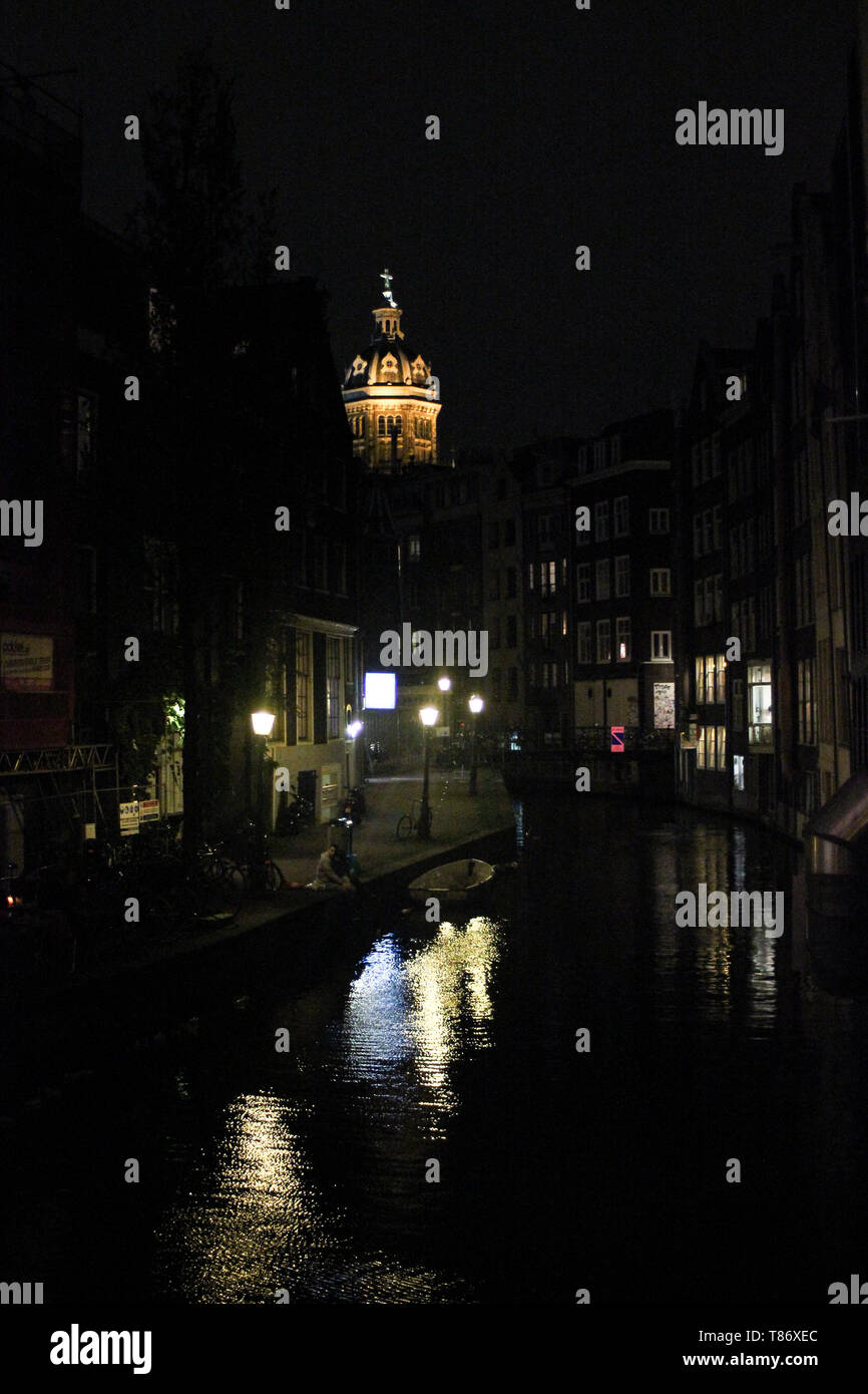 Réflexions de l'éclairage de rue sur canal. Basilique de Saint Nicolas lumineux sur l'arrière-plan. Amsterdam, Pays-Bas. Banque D'Images