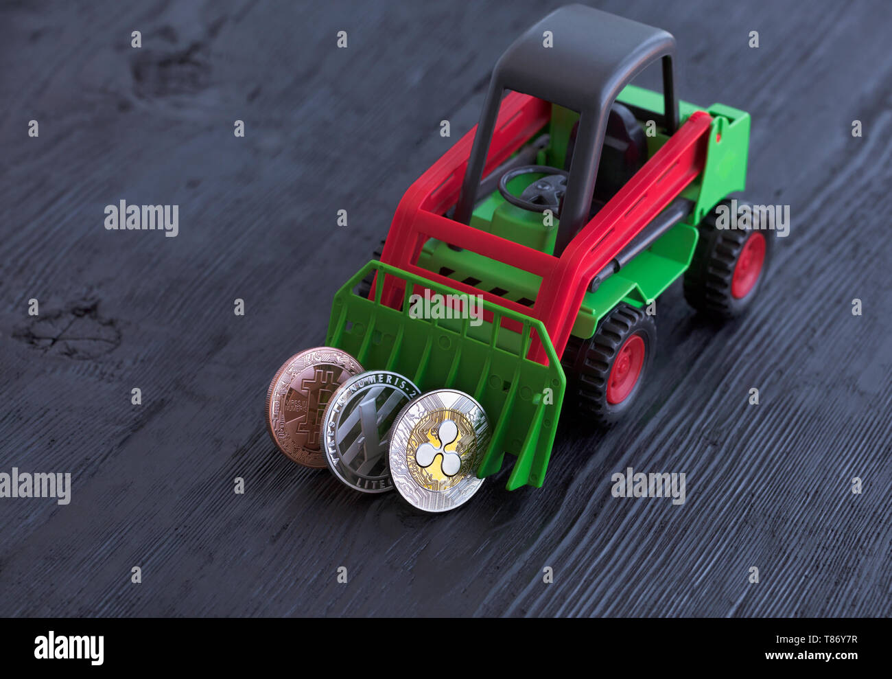 Un jouet tracteur pièces râteaux de crypto monnaie sur un fond en bois  noir, bitcoin : lightcoin, ondulation. Le concept du jeu avec crypto- monnaies Photo Stock - Alamy